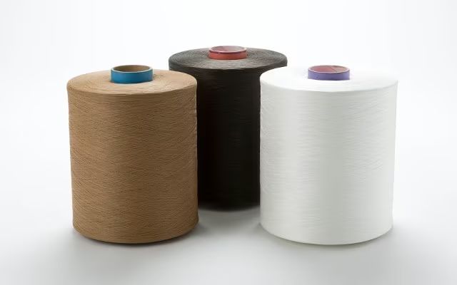 Three spools of yarn: tan, black, and white. Each has a colored cap.