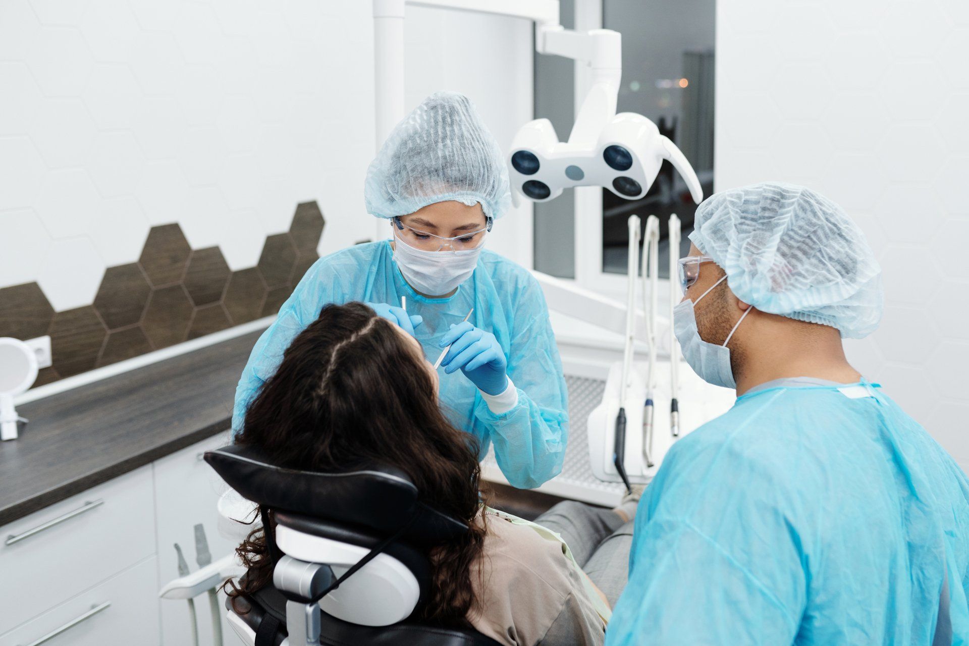 A woman is sitting in a dental chair getting her teeth examined by two dentists.