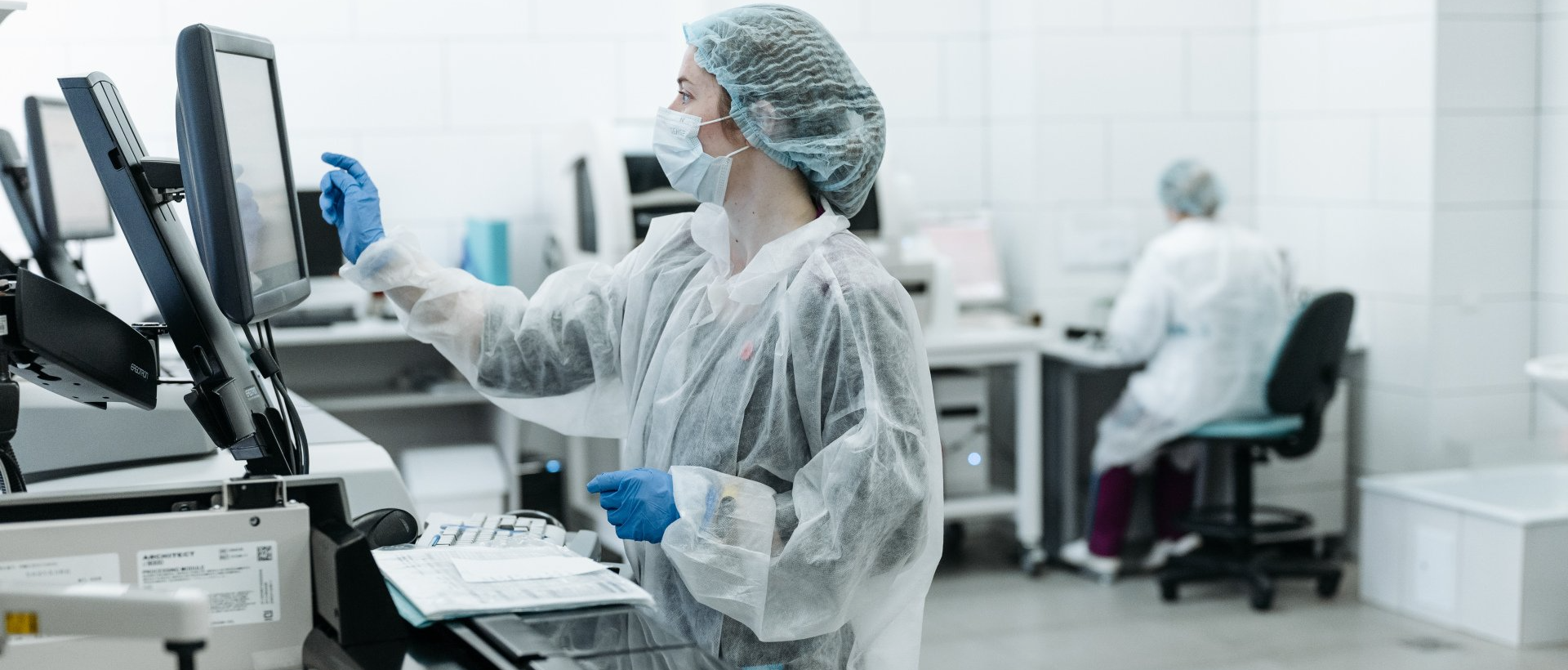 A woman in a protective suit is working on a computer in a laboratory.