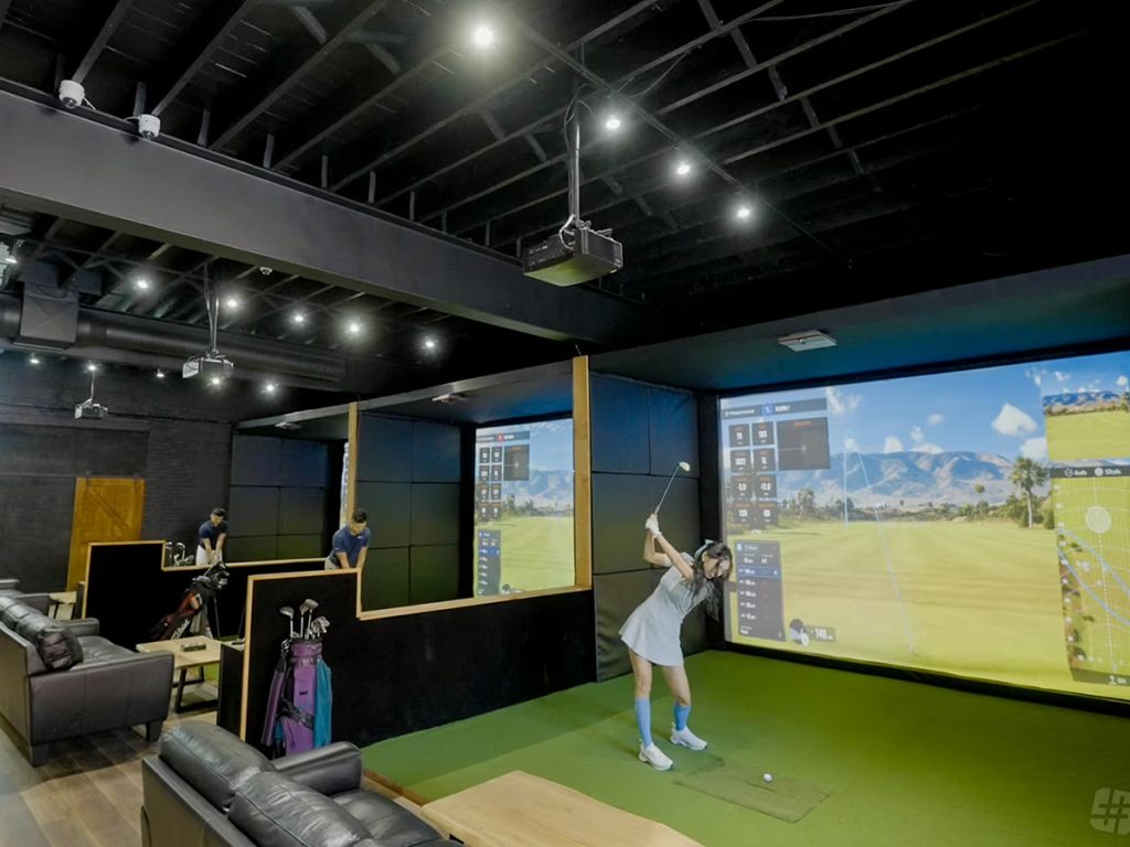 Woman drives a golf ball into a screen at a commercial golf simulator