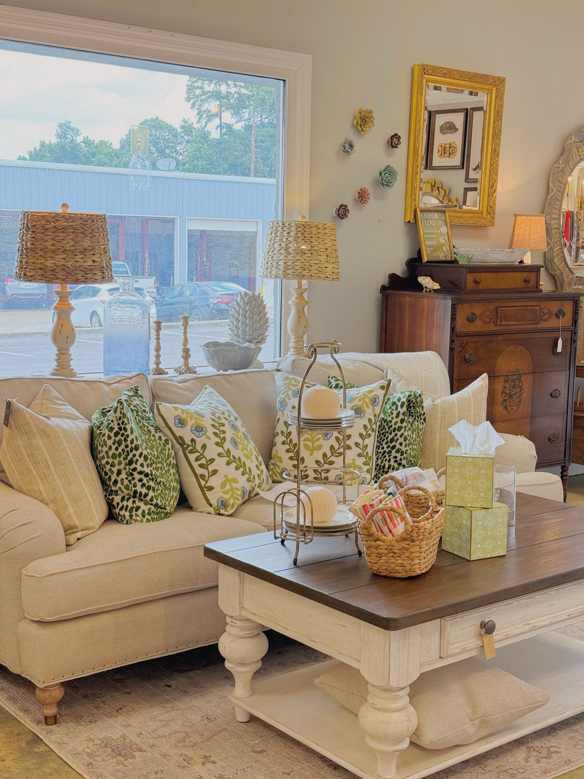 Cozy living room with cream sofa, patterned pillows, coffee table, lamps, and a wooden dresser by the window