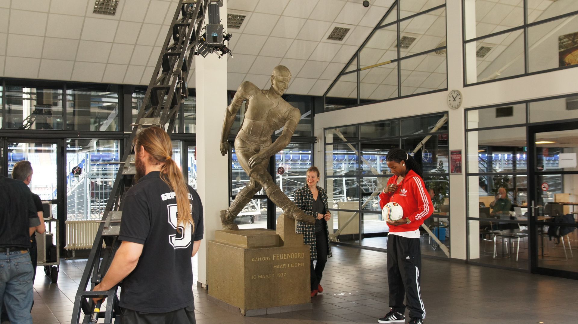 Mensen lopen rond een groot standbeeld in een atrium met glazen wanden.