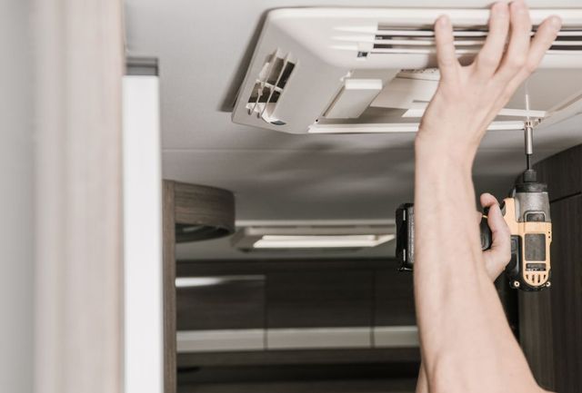 Person using a drill to install an air conditioner in a recreational vehicle.