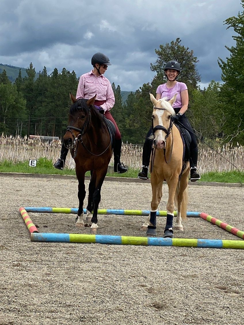Two women are riding horses in a dirt field.