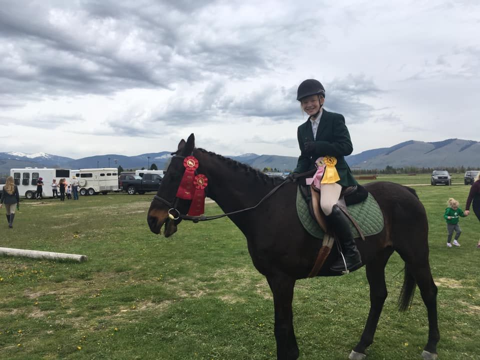 A woman is riding a horse in a field with mountains in the background.