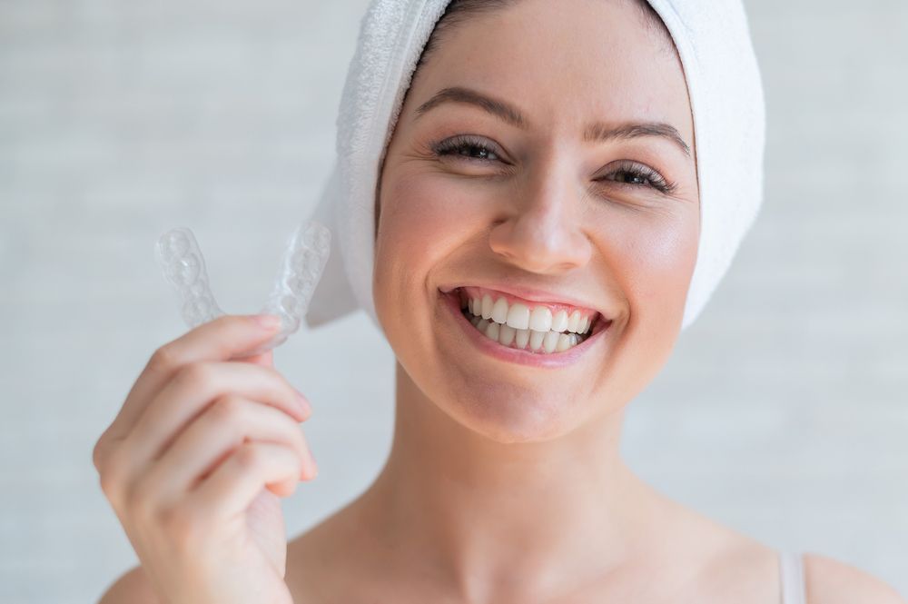 a woman with a towel wrapped around her head is smiling and holding a clear teeth brace