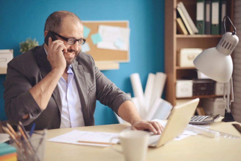 Man working at desk with a laptop in office talking on phone