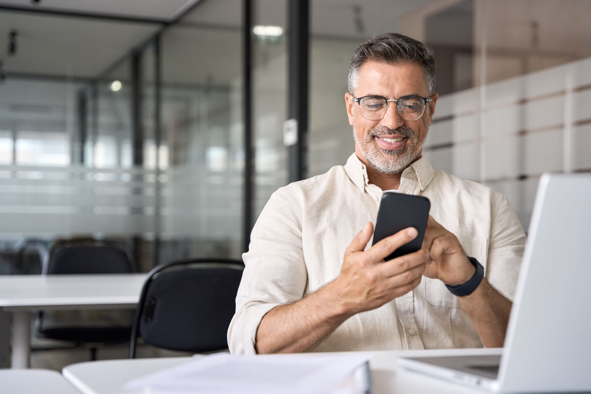 a man is sitting at a desk looking at his cell phone .