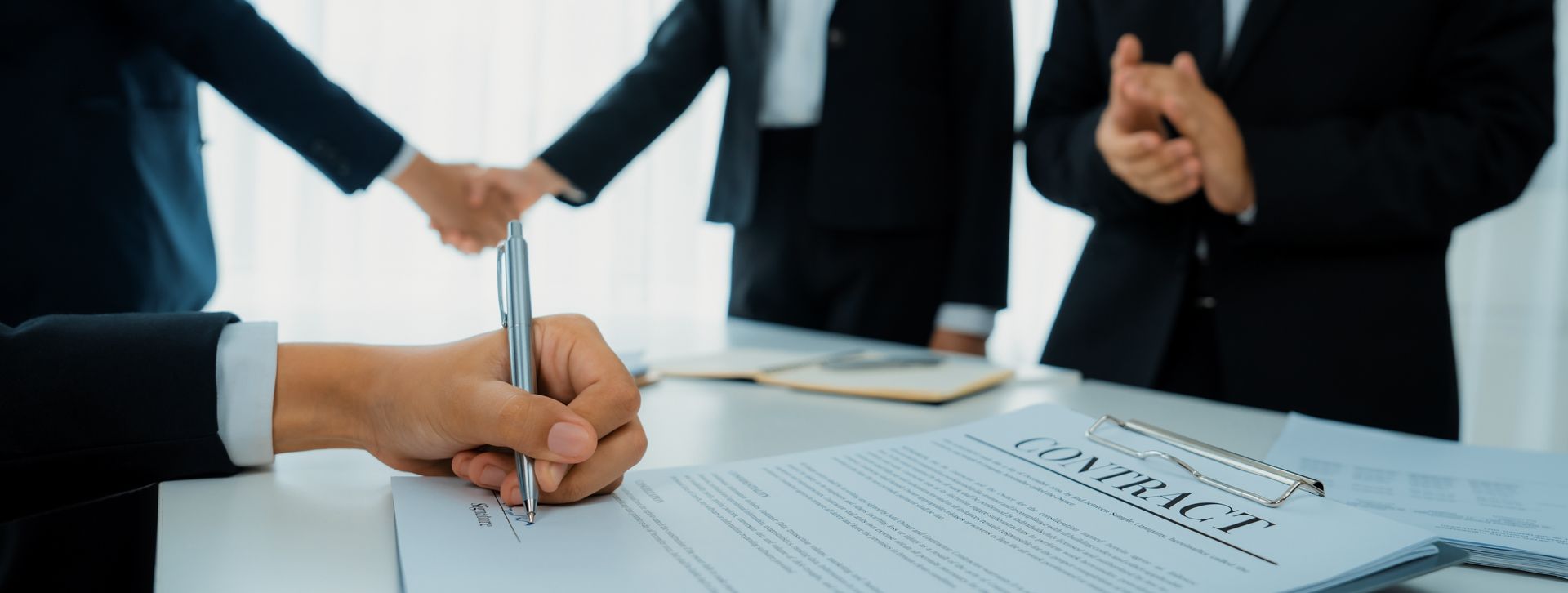 a group of business people are shaking hands and signing a contract .