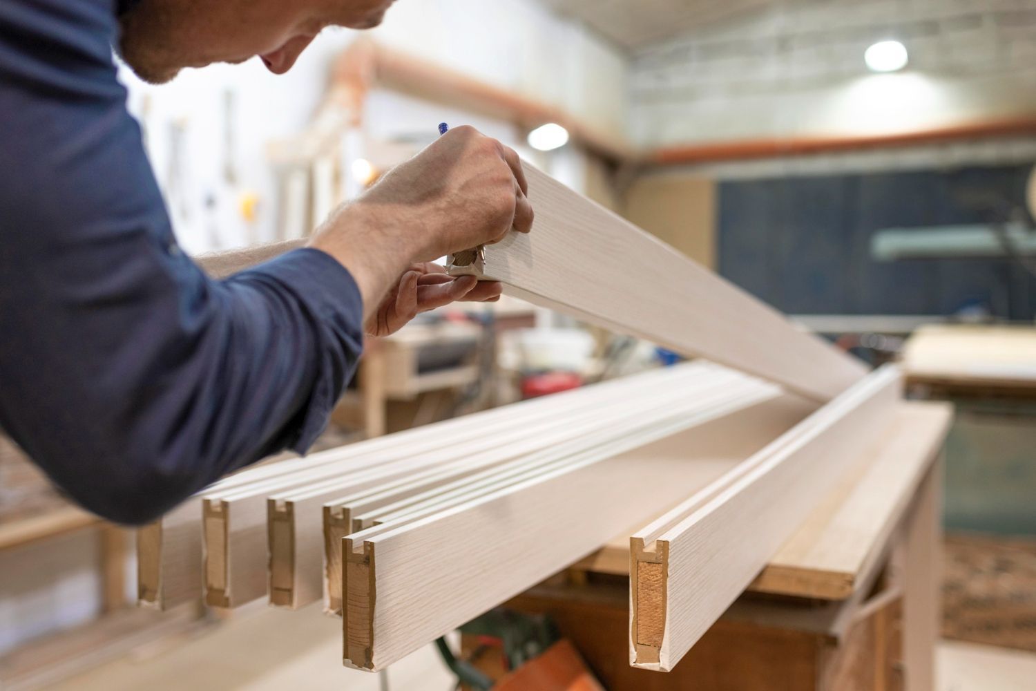 A man is measuring a piece of wood in a workshop.