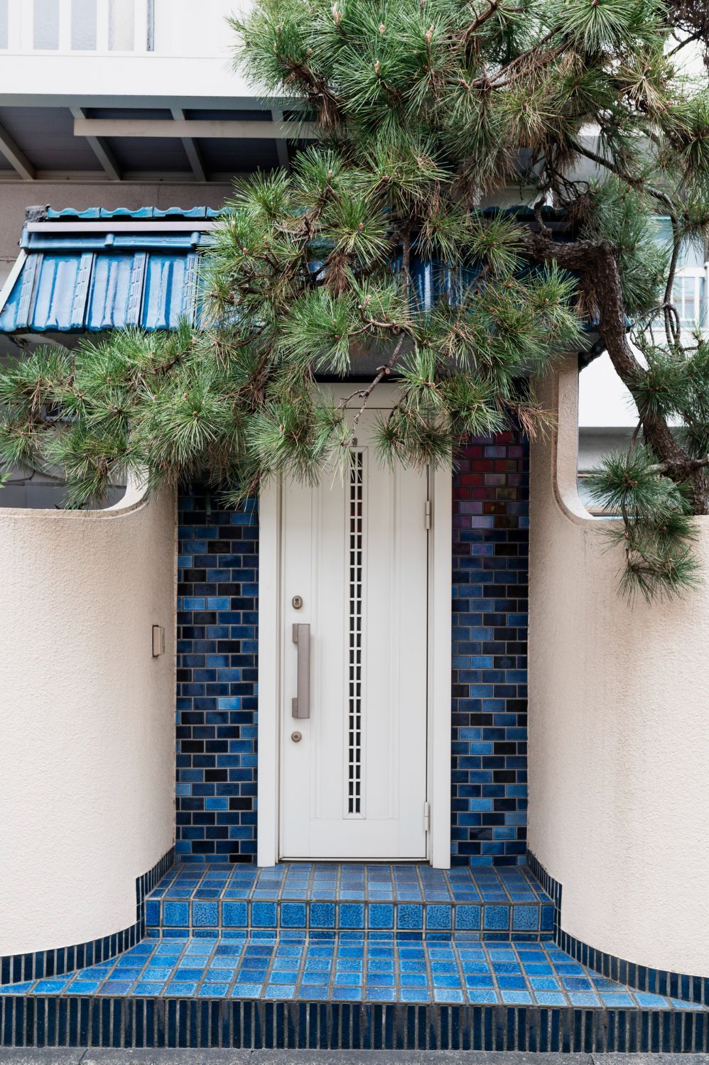 White door framed by blue tiles and a pine tree.