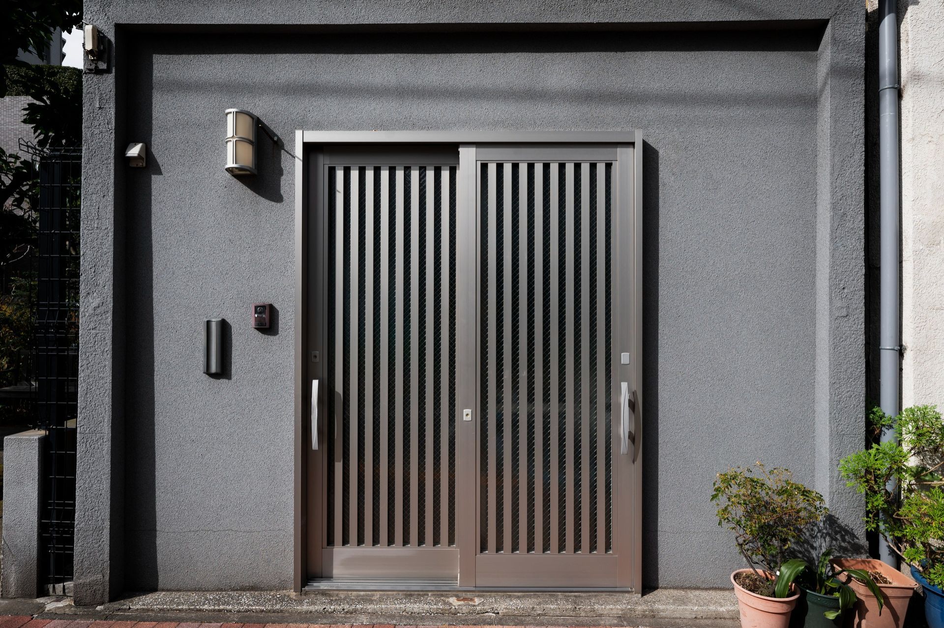 A gray building with a sliding door and potted plants in front of it.