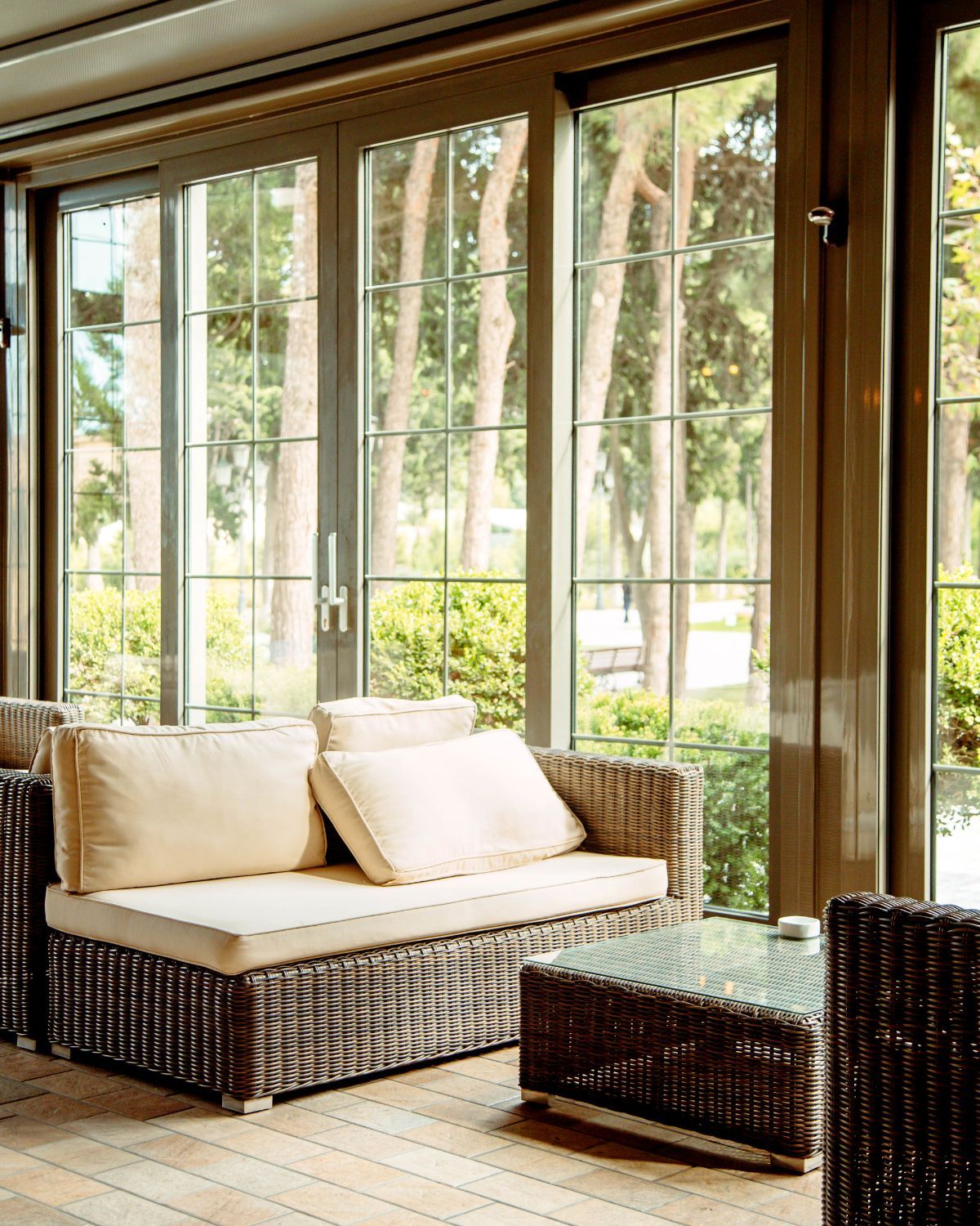 Wicker seating near large windows overlooking trees; neutral tones.