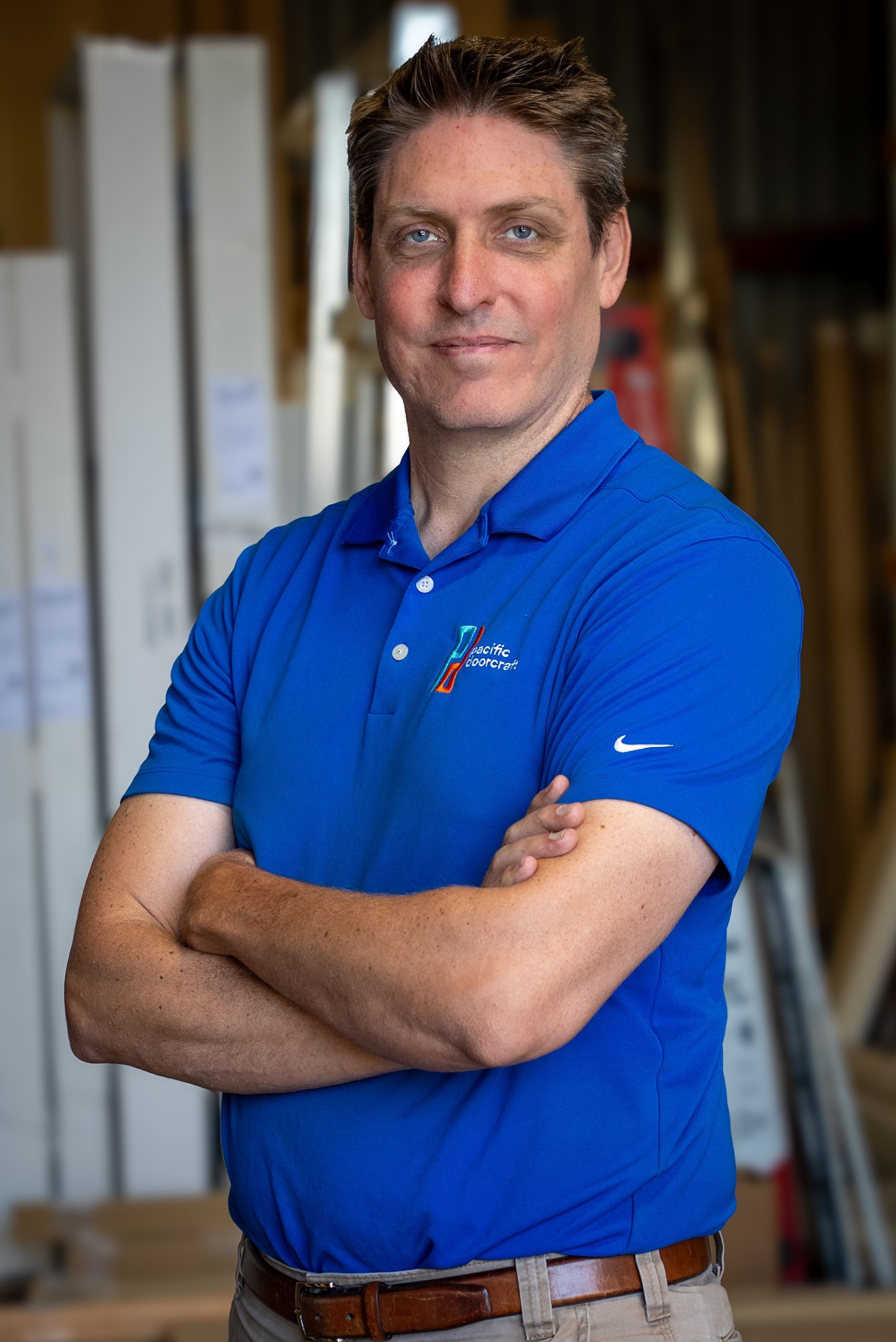 Man in blue polo shirt with arms crossed, in a workshop setting.