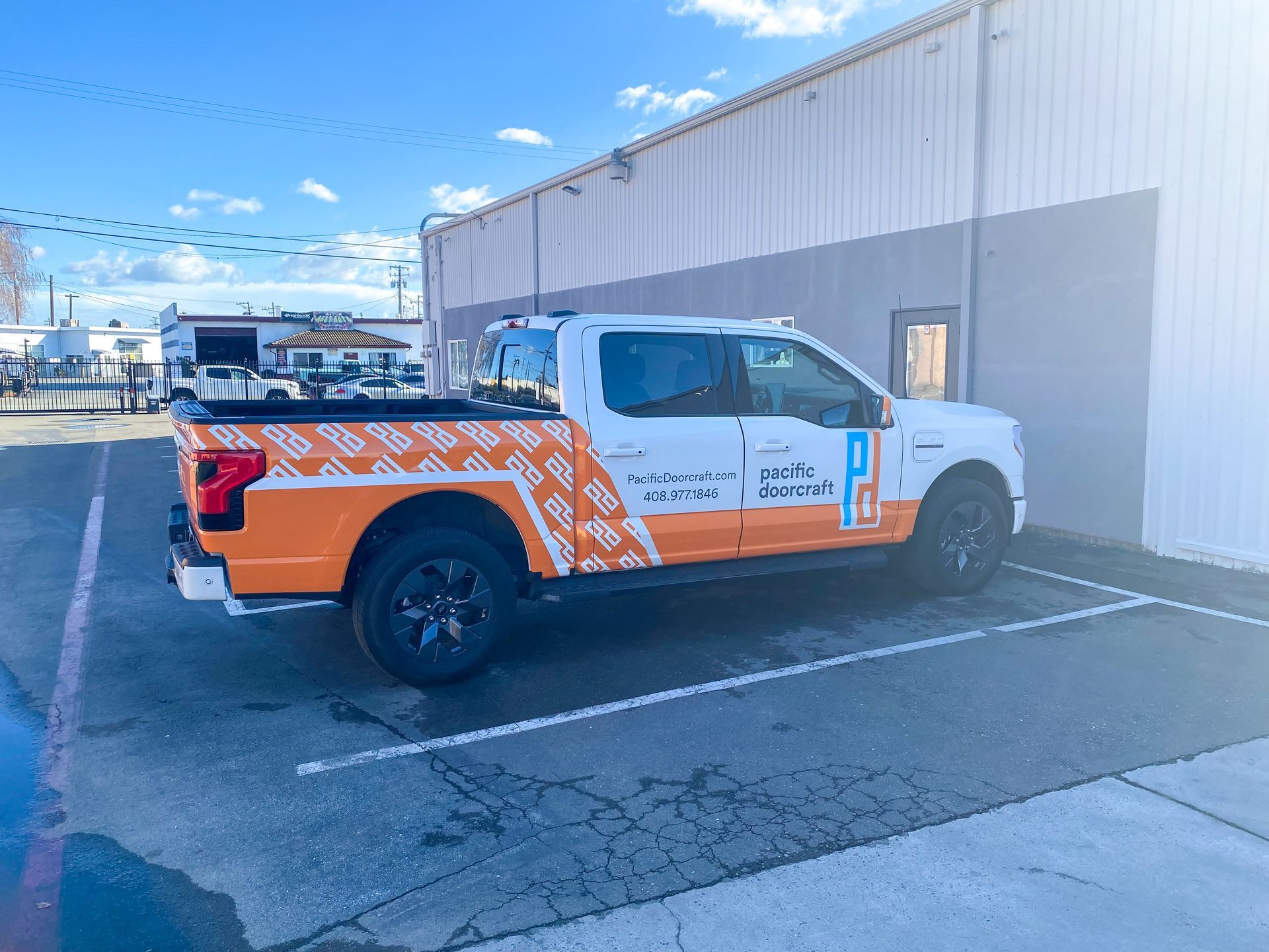 A white and orange truck is parked in a parking lot in front of a building.