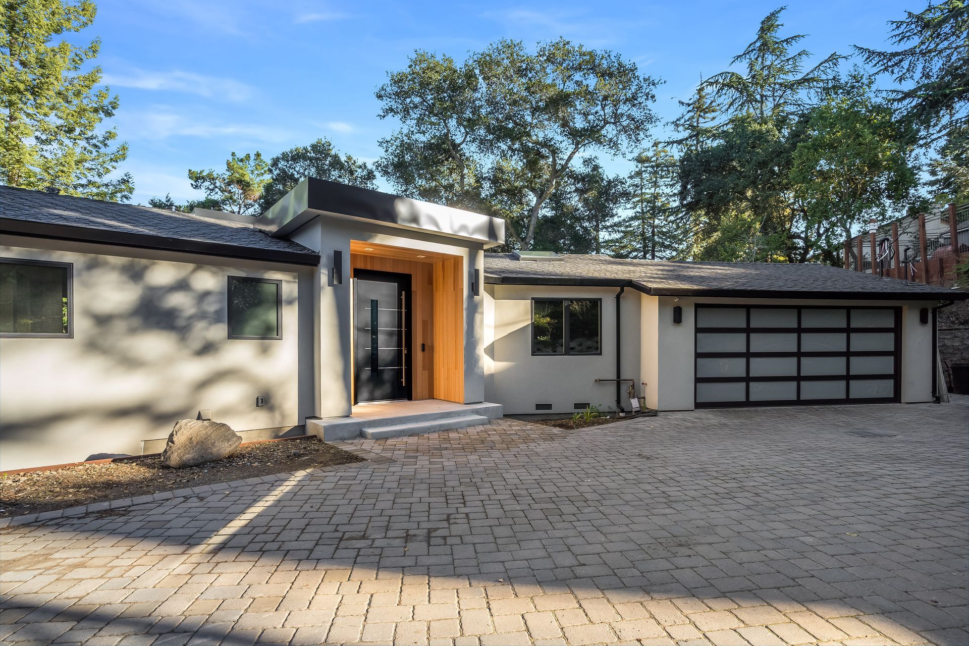 A white house with a black garage door and a brick driveway