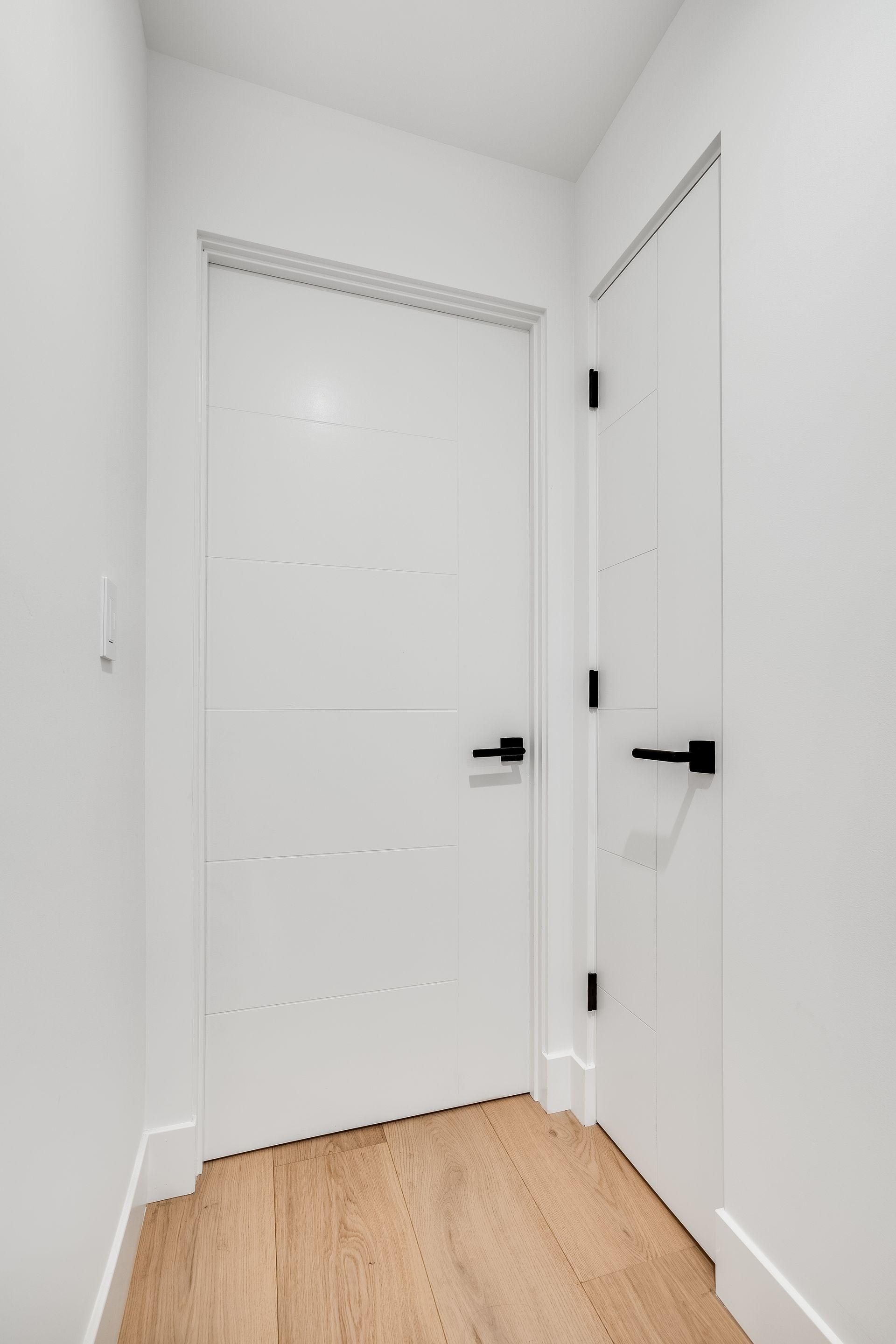 A hallway with a white door and wooden floor.