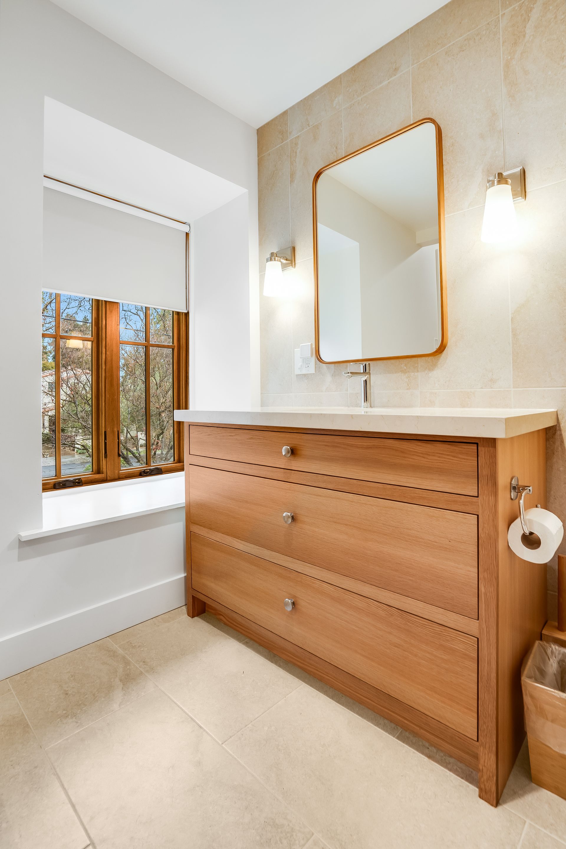 A bathroom with a wooden vanity , sink , mirror and window.
