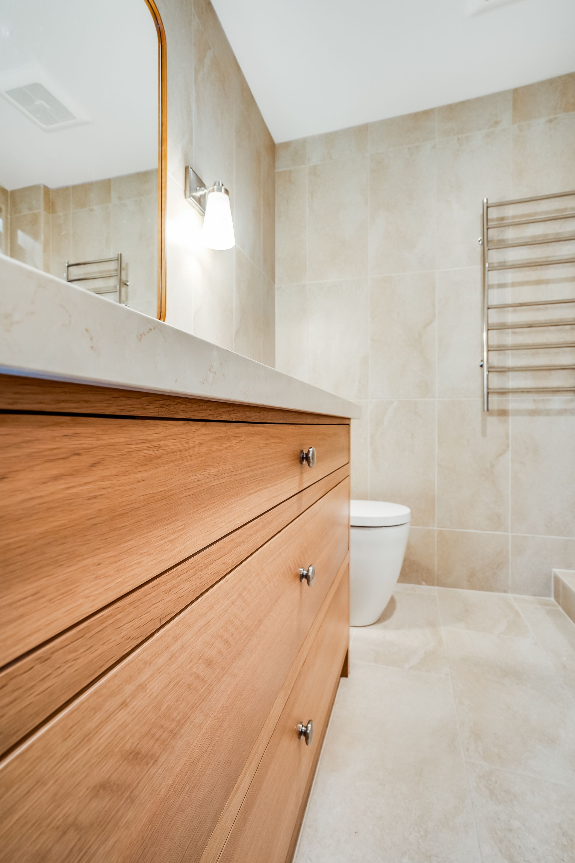 A bathroom with a wooden vanity , toilet , mirror and towel rack.
