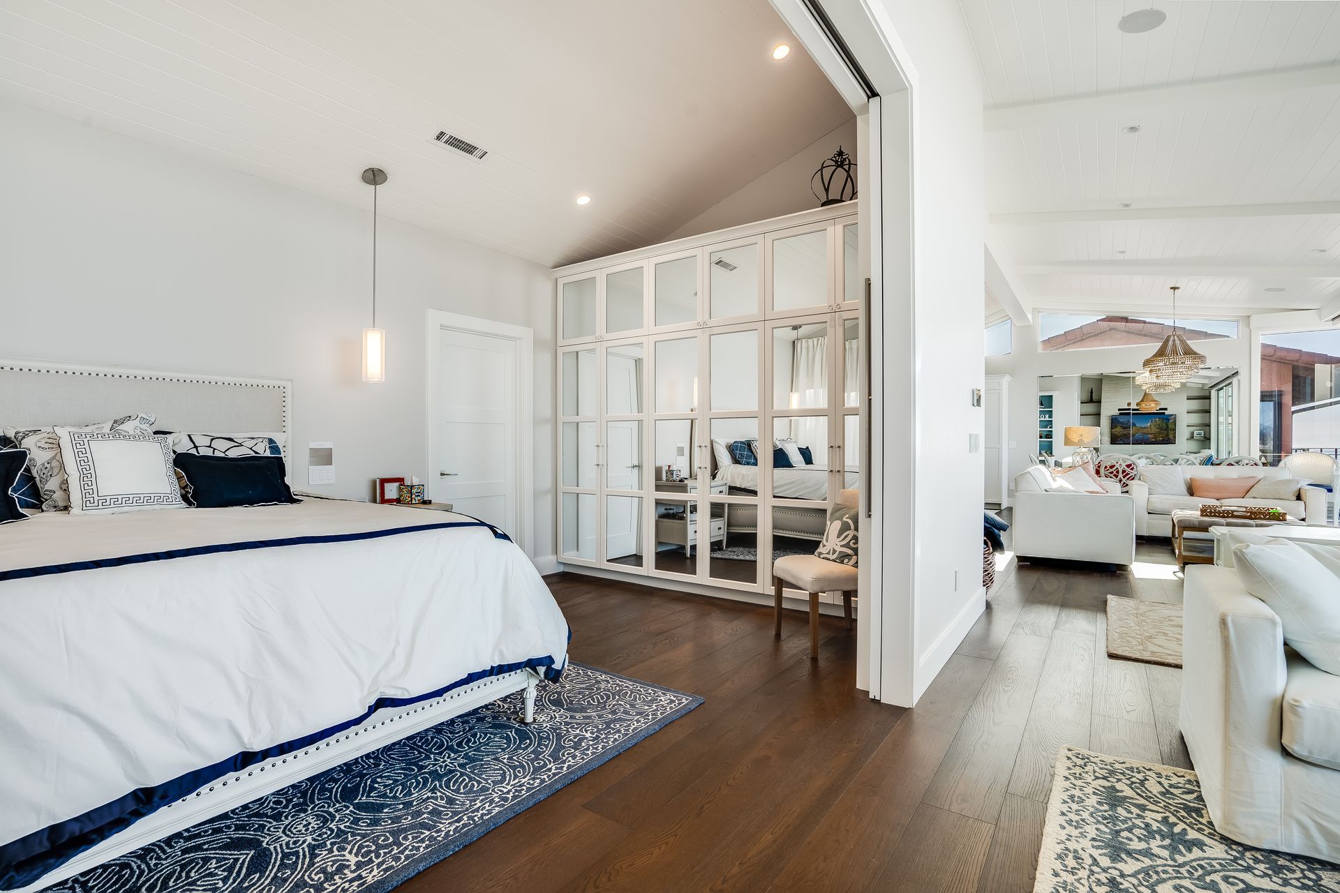 A bedroom with a large bed and a sliding glass door between the bedroom and living room.