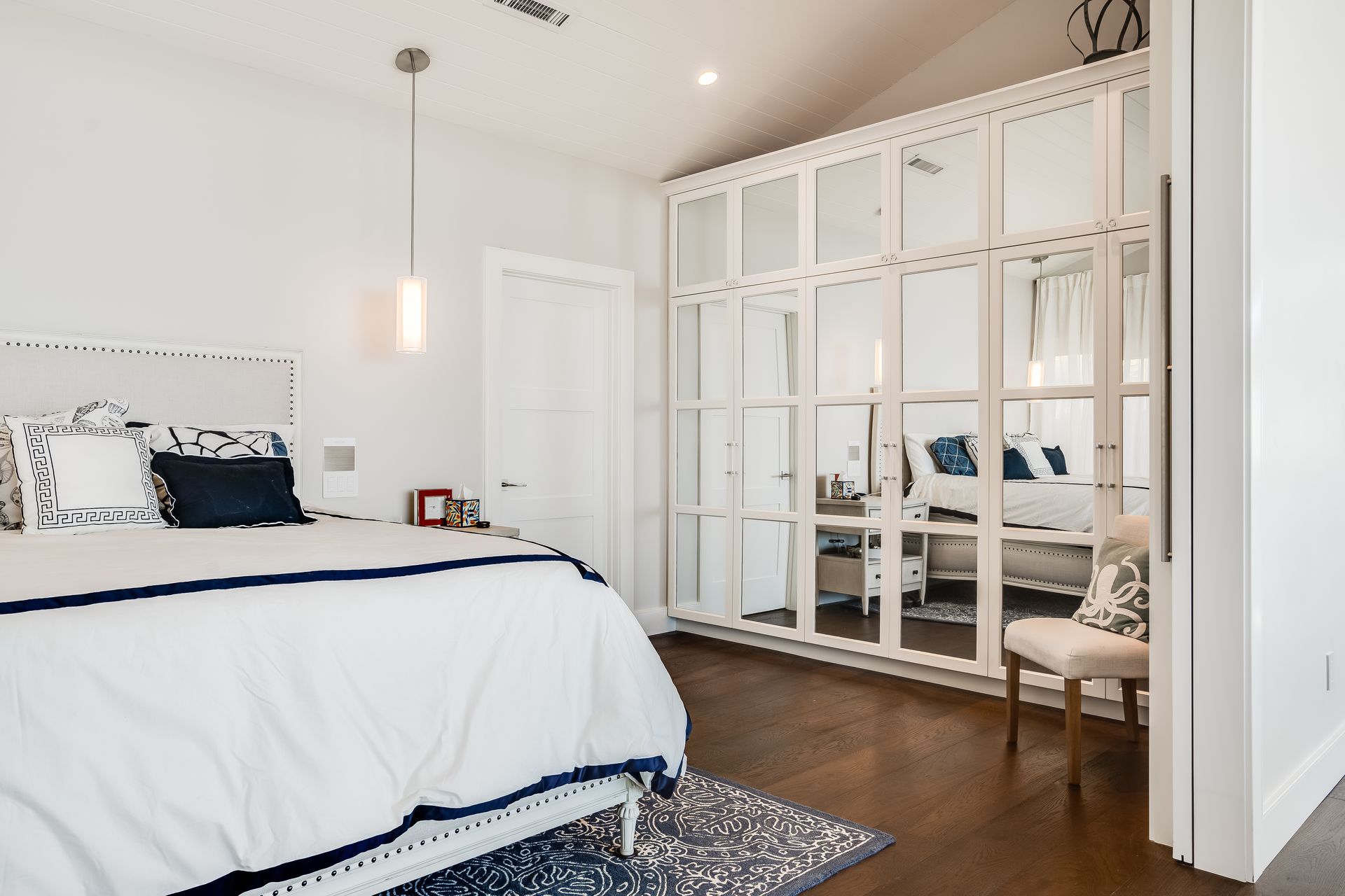 A bedroom with a bed , chair , and mirrored cabinets.