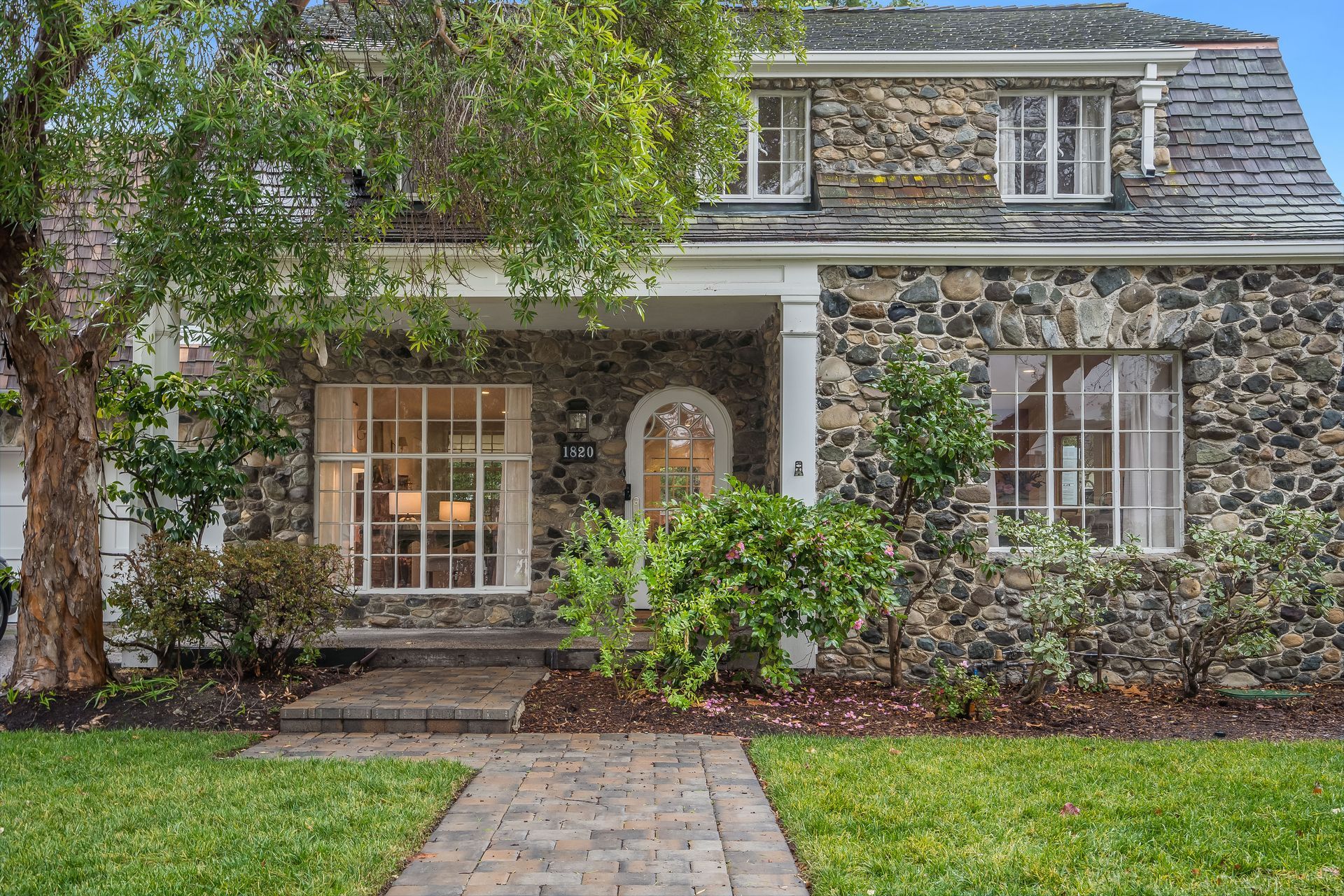 The front of a stone house with a brick walkway leading to it.