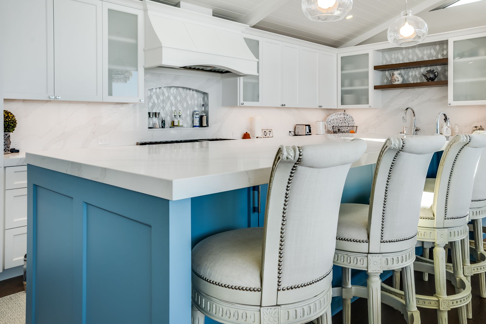 A kitchen with a blue island and white chairs.