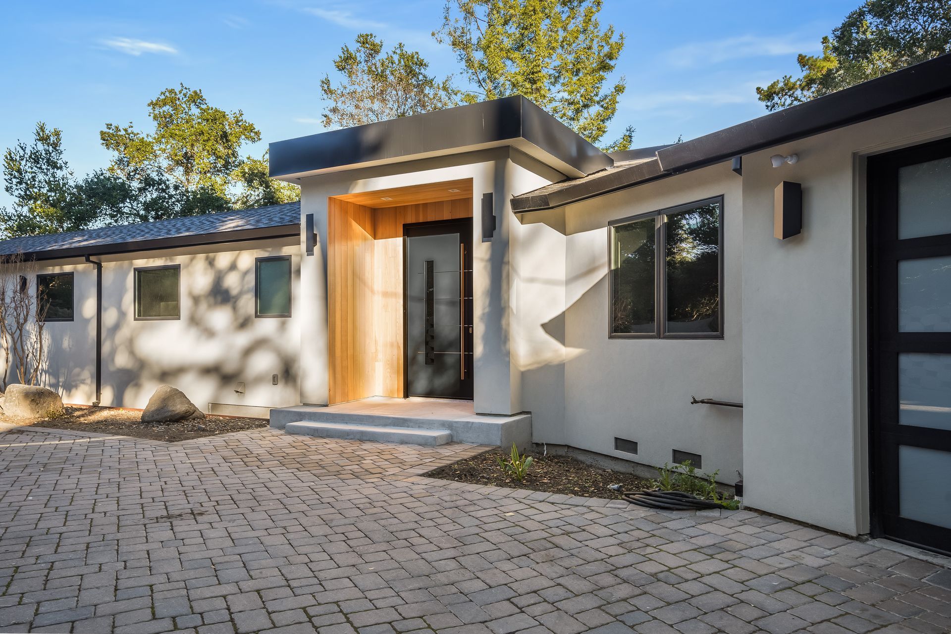 A white house with a black garage door and a brick driveway.