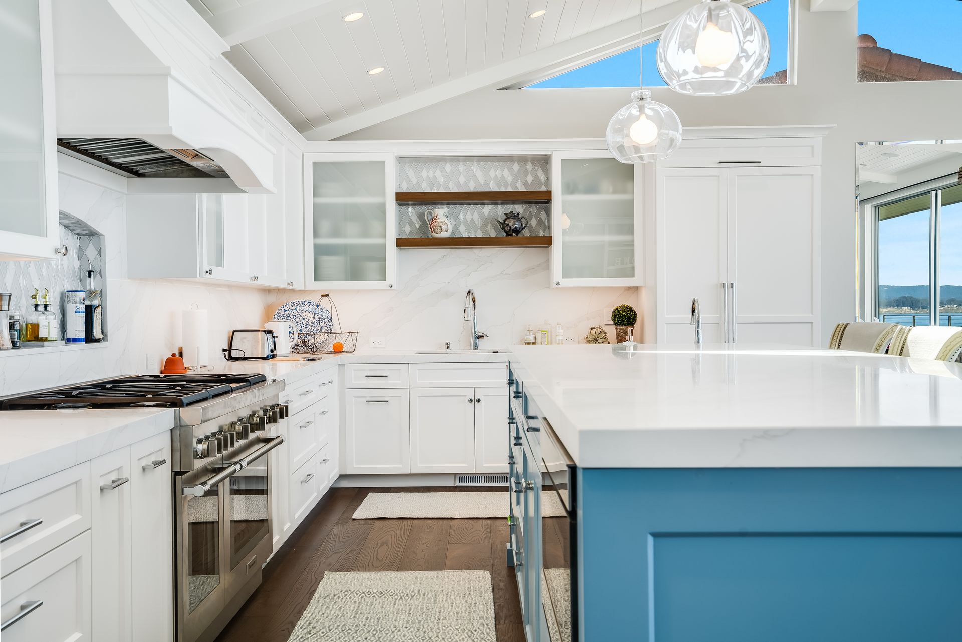 A kitchen with white cabinets , stainless steel appliances , and a blue island.