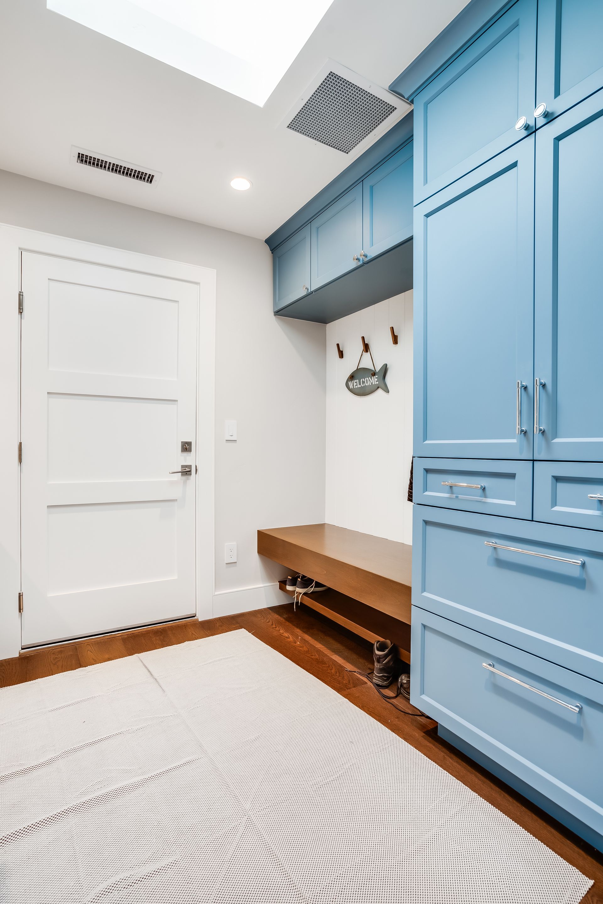 A hallway with blue cabinets , a bench , and a rug.