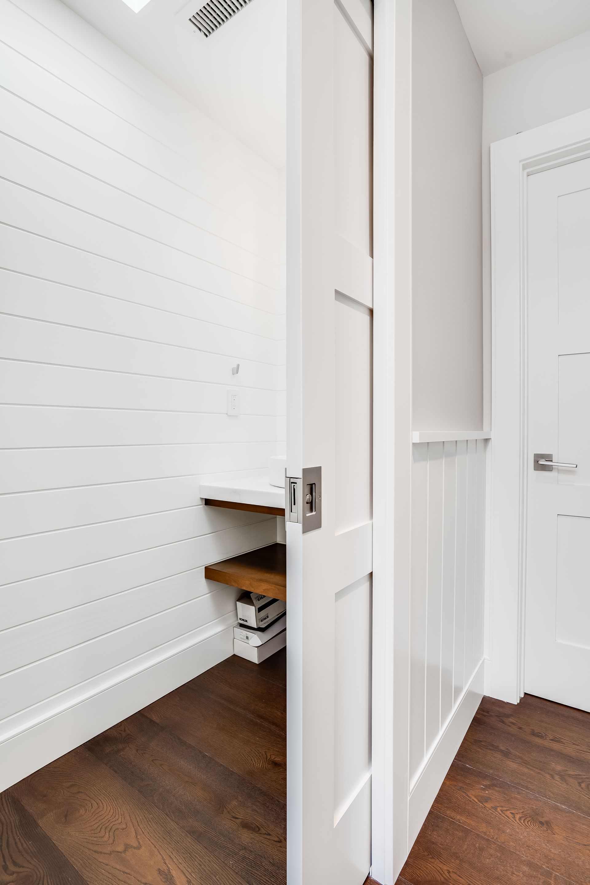 A walk in closet with white walls and a wooden floor.