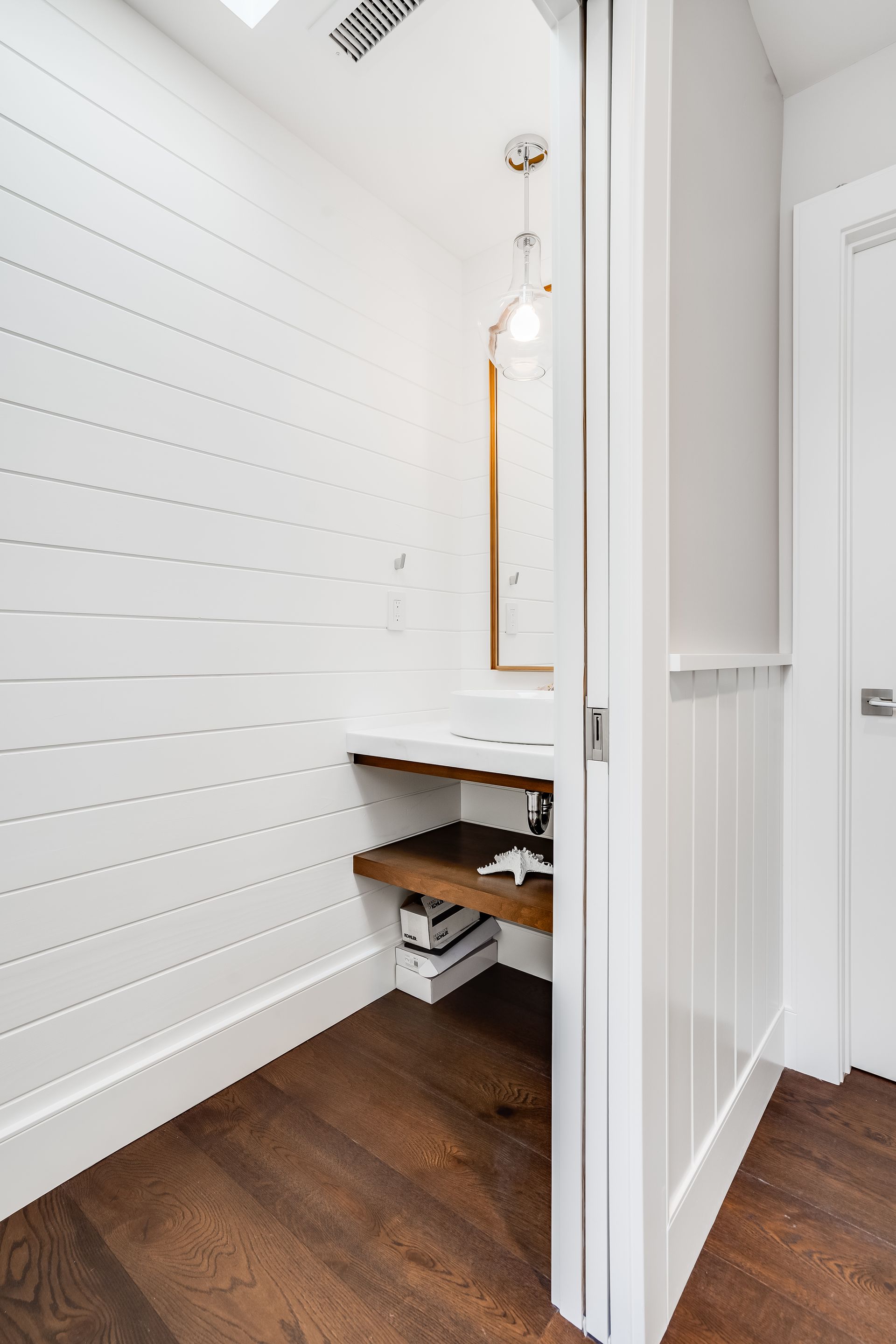 A bathroom with white walls and wooden floors and a sink.