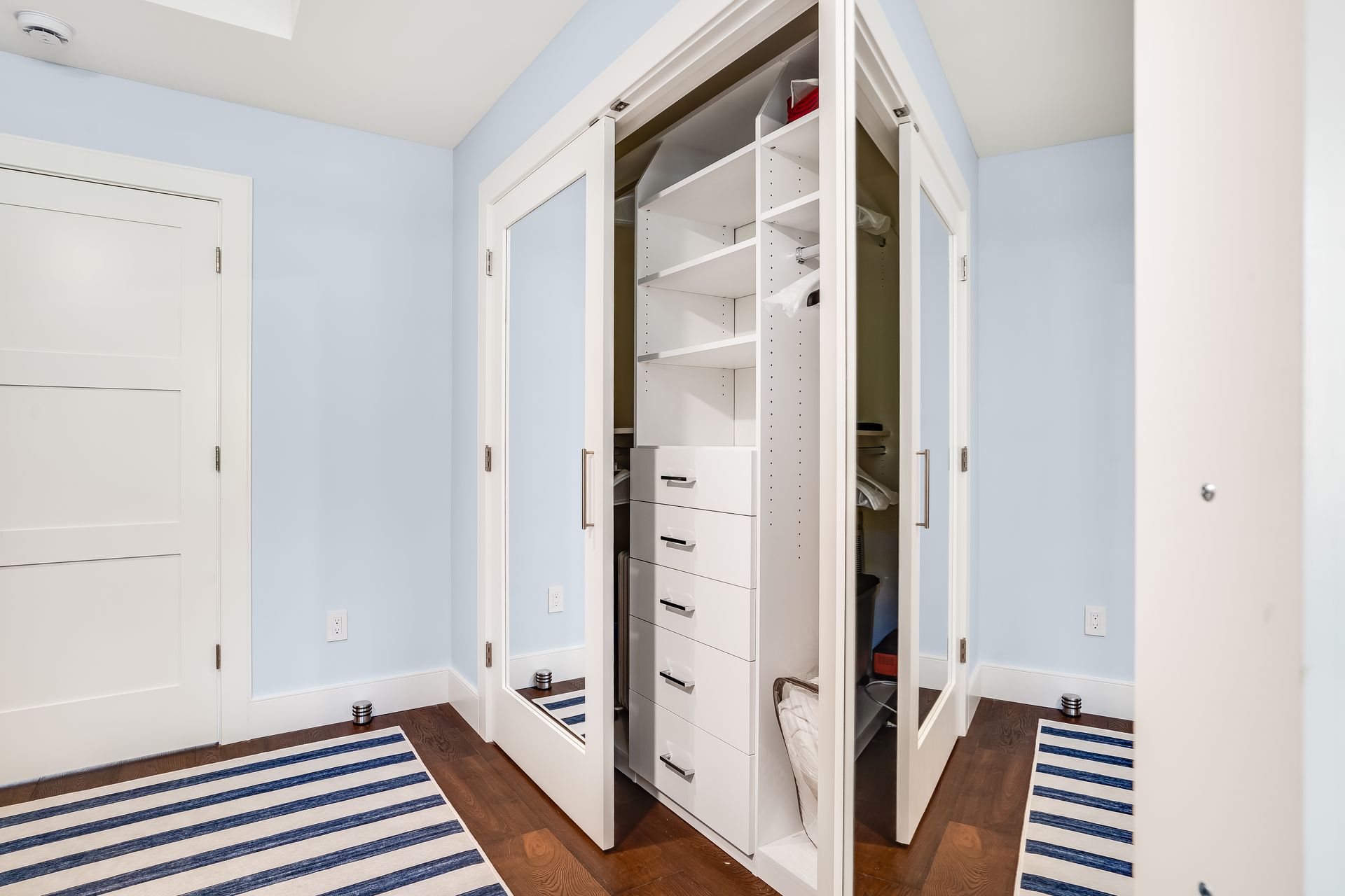 A walk in closet with a striped rug and mirrored doors.