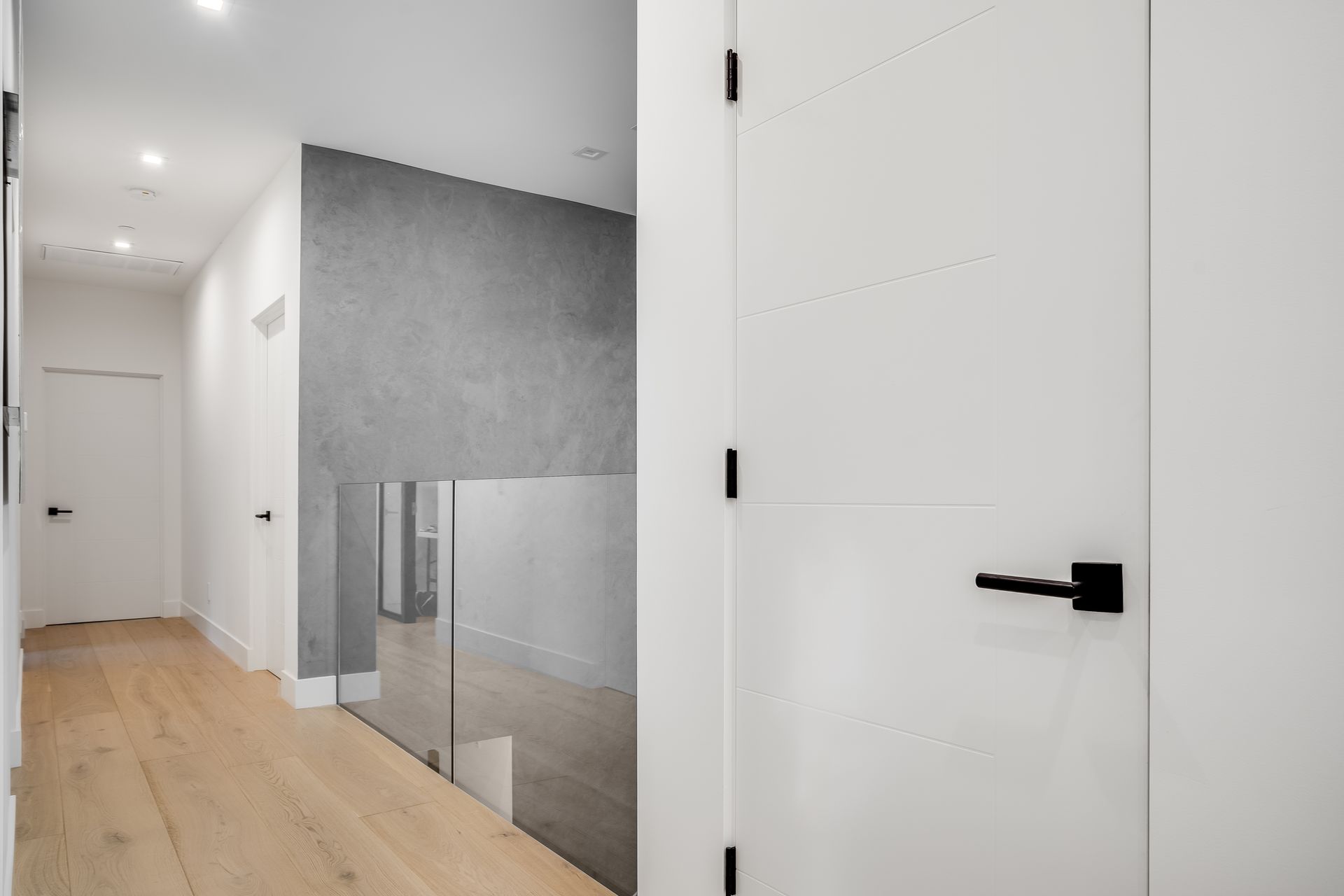 A hallway with a glass railing and a white door leading to a staircase.