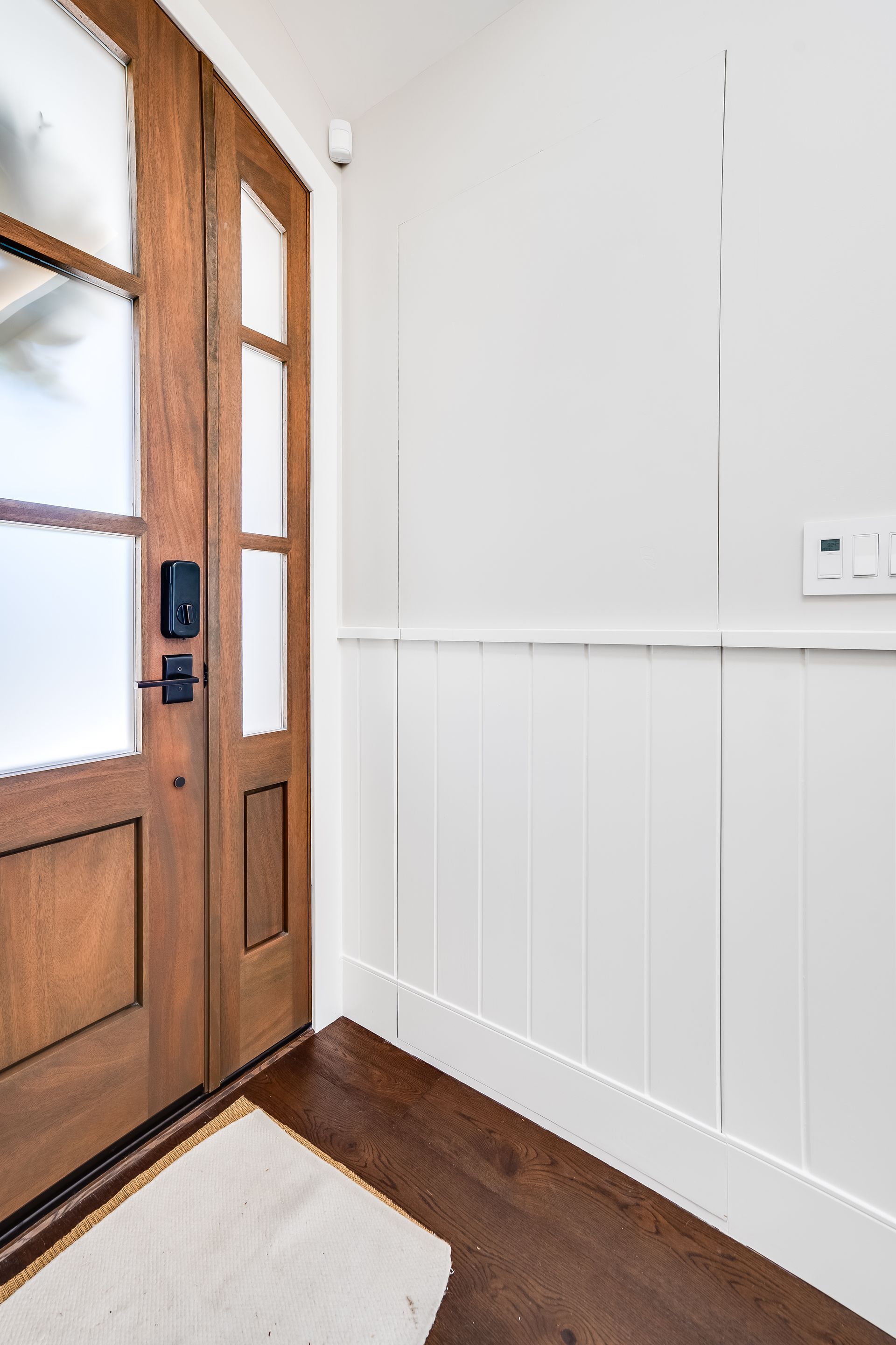 A wooden door with a glass window is in a hallway next to a white wall.