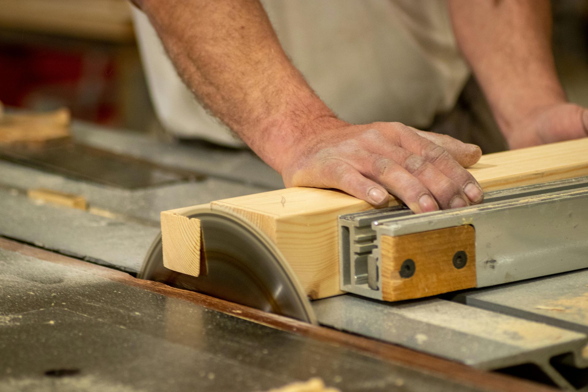 A man is cutting a piece of wood on a table saw.