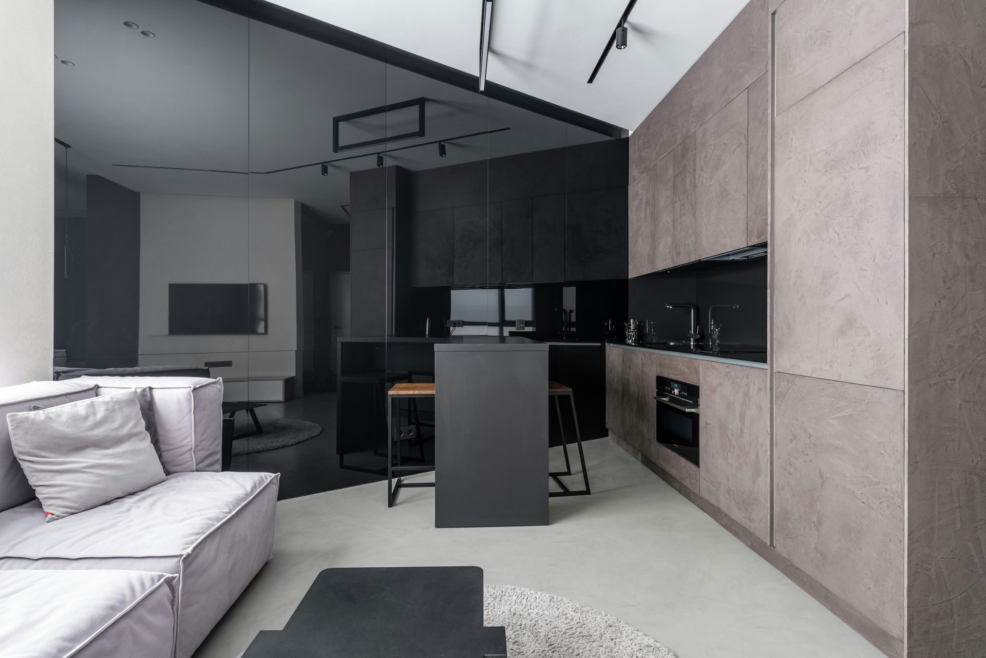 A living room with a couch and a kitchen with black cabinets.