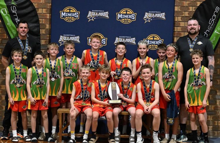 Youth basketball team in green and red uniforms posing with coaches on a gym court.