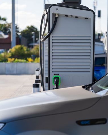 Electric vehicle charging station behind a parked silver car outdoors.