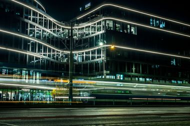 Blurred nighttime city street with modern glass office buildings and light trails from passing traffic