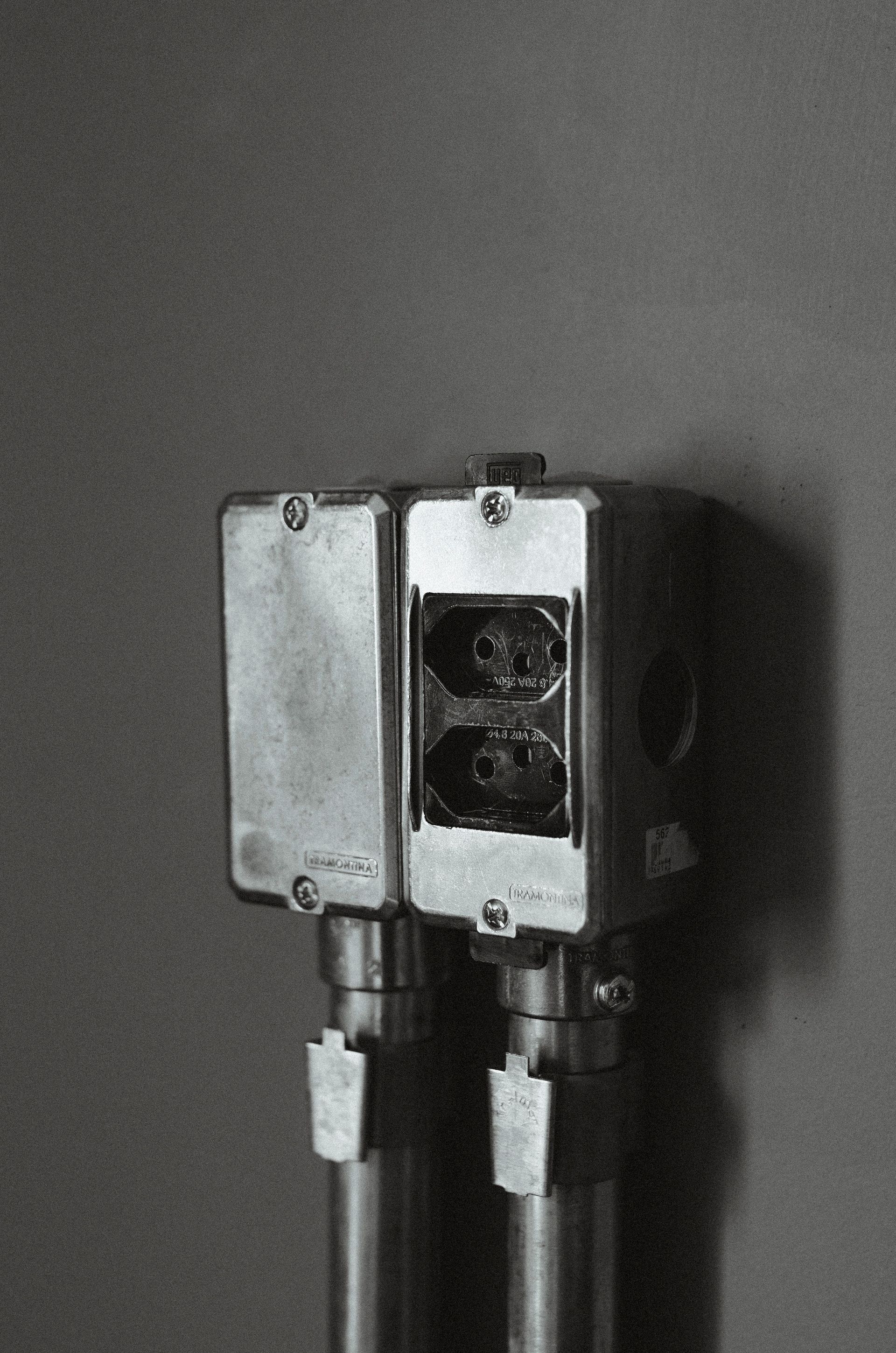 Outdoor electrical outlet box mounted on a wall, with two plugs connected and a cover open.