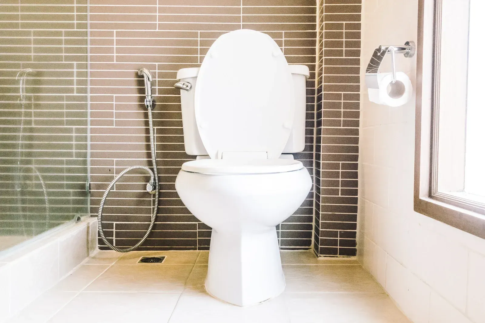 A white toilet is sitting in a bathroom next to a window.