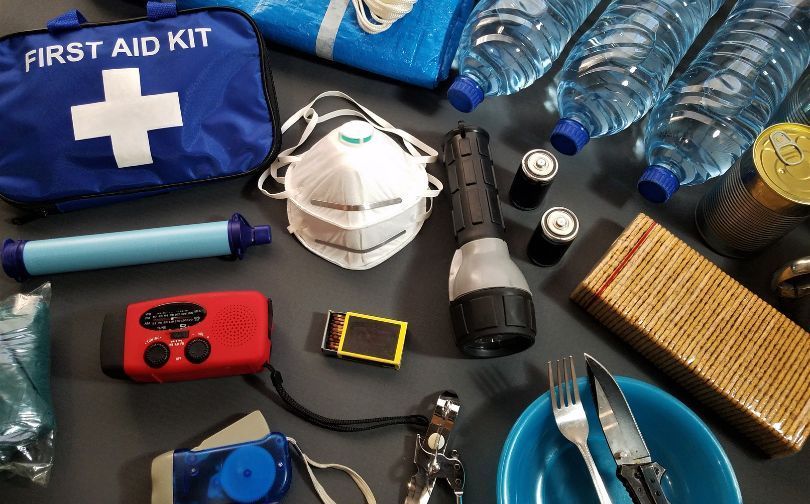 Emergency supplies laid out on a table, including a first aid kit, flashlight, mask, water bottles, and tools