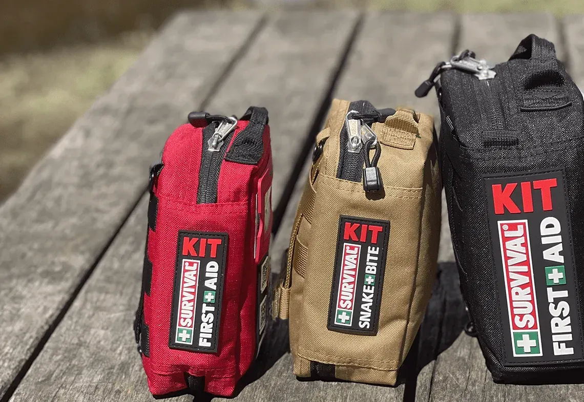Three first-aid kits in red, tan, and black on a wooden surface.