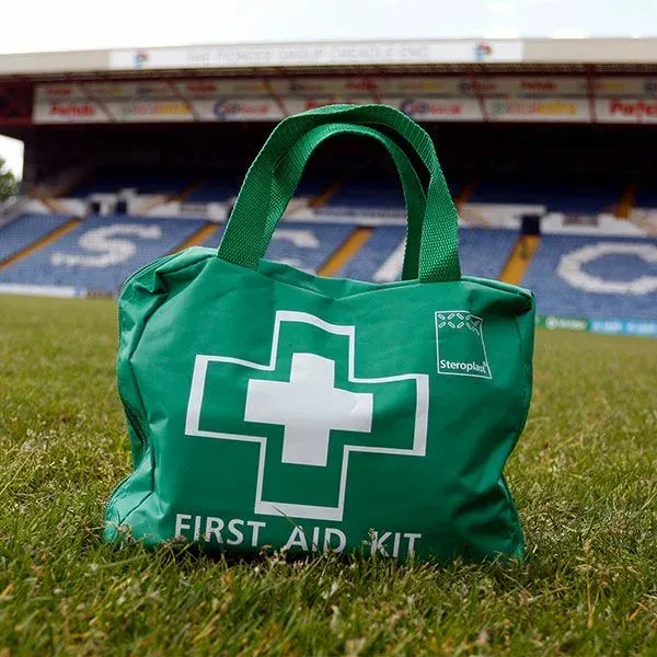 Green first aid kit bag with white cross on grass in a stadium