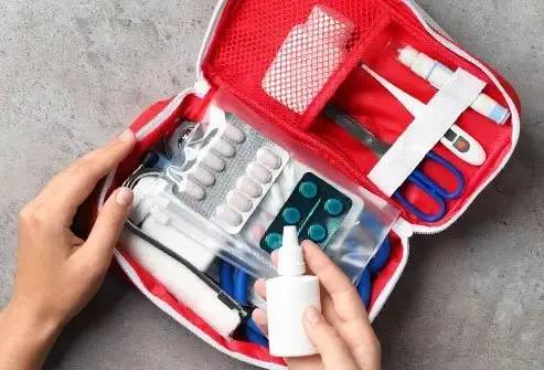 Open first aid kit with bandages, pills, and medicine being organized by hands