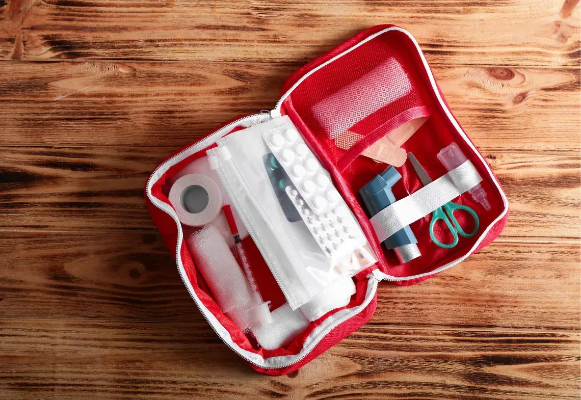 Open red first-aid kit with bandages and medical supplies on a wooden table