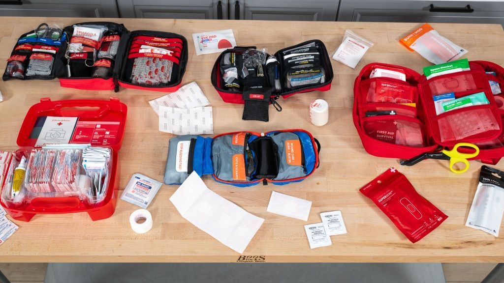 Assorted red and black emergency kits and supplies spread across a wooden table