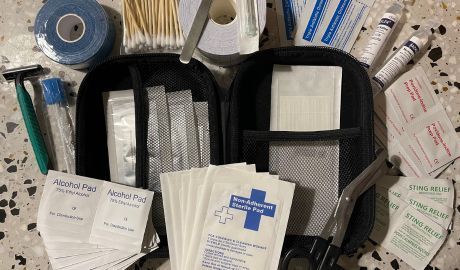 Medical supplies laid out on a tabletop, including a bag, gauze pads, tape, and packaged dressings.