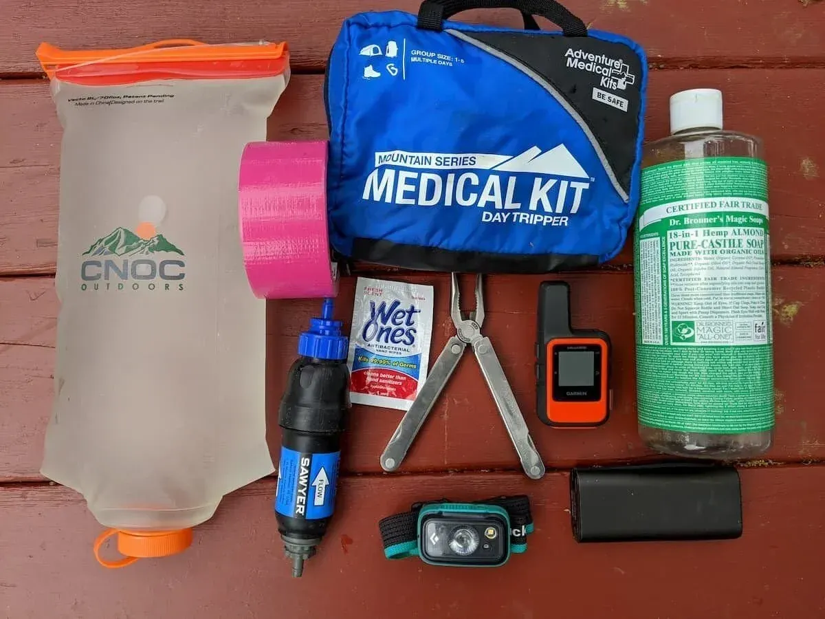 Emergency kit items laid out on a red surface, including a water pouch, medical kit, flashlight, and sanitizer.
